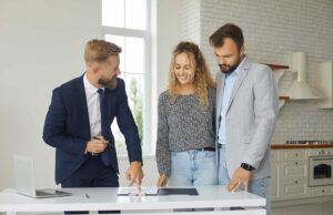 A couple reviews a thick stack of real estate closing documents with a pen and calculator at their dining table.